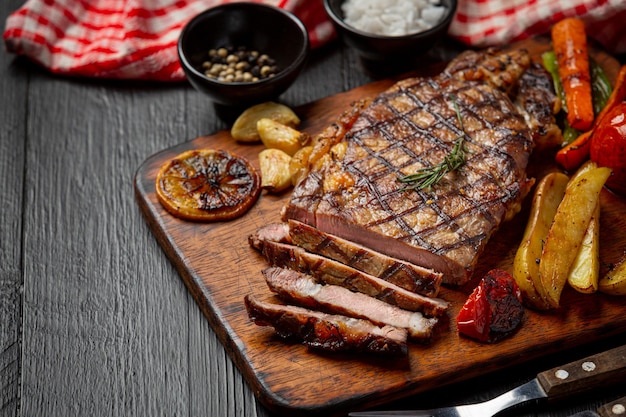 Grilled beef steak on the dark wooden surface.