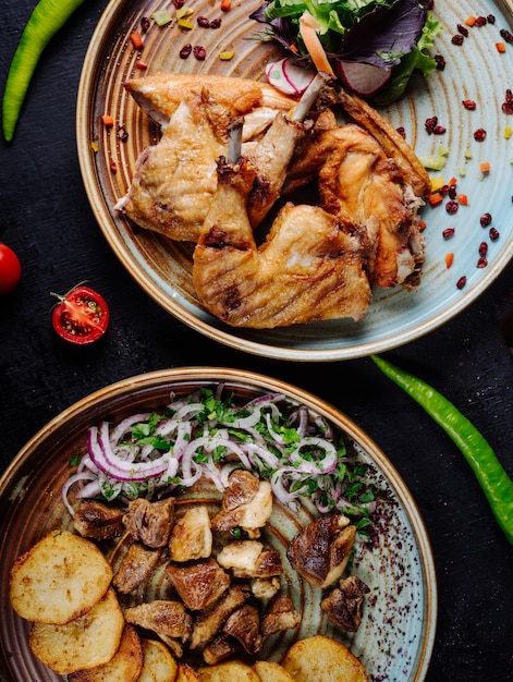 Pollo alla griglia, spezzatino di manzo e patatine fritte con cipolla e insalata verde nei piatti.