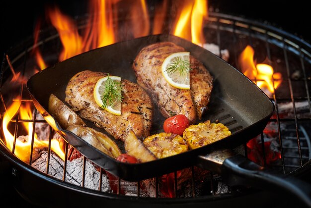 Grilled chicken breast on the flaming grill with Grilled vegetables tomatoes, herbs, lemon, rosemary. Healthy lunch menu.