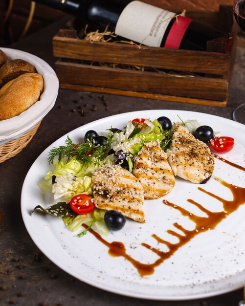 Grilled chicken breast served with vegetable salad and olives