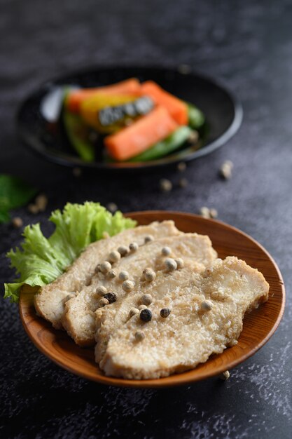 Grilled chicken breast, sprinkled with pepper, placed on a wooden plate