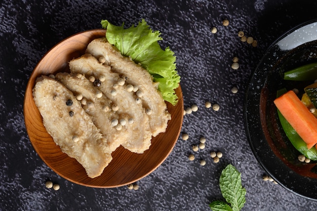 Grilled chicken breast, sprinkled with pepper, placed on a wooden plate