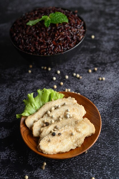 Grilled chicken breast, sprinkled with pepper, placed on a wooden plate