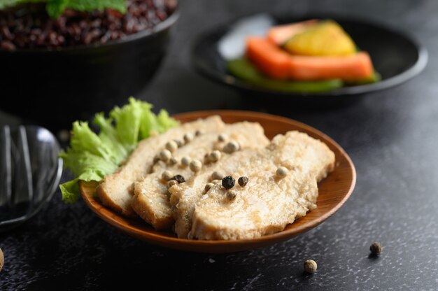 Grilled chicken breast, sprinkled with pepper, placed on a wooden plate