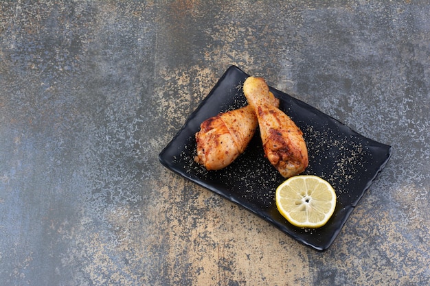 Grilled chicken drumsticks on black plate with lemon. High quality photo