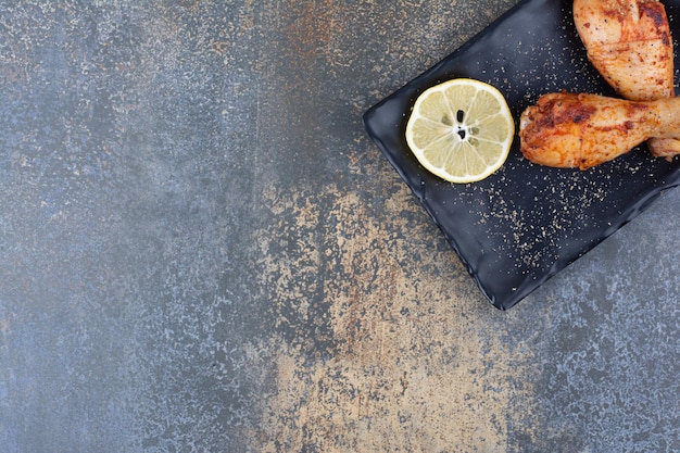 Жареные куриные голени на черной тарелке с лимоном. Фото высокого качества
