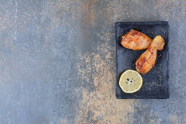 Free photo grilled chicken drumsticks on black plate with lemon.