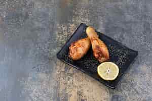 Бесплатное фото Жареные куриные голени на черной тарелке с лимоном. фото высокого качества