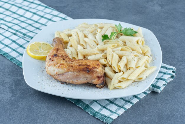 Grilled chicken leg and penne pasta on white plate.