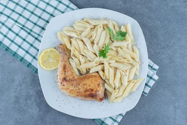 Grilled chicken leg and penne pasta on white plate. 