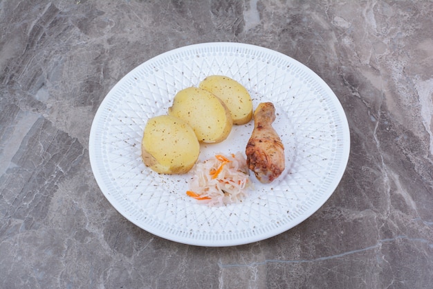 Жареная куриная ножка, картофель и квашеная капуста на белой тарелке.