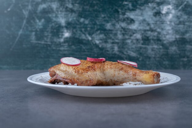 Жареная куриная ножка и нарезанный редис на белой тарелке.