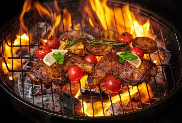 Grilled chicken legs on the flaming grill with grilled vegetables with tomatoes, potatoes, pepper seeds, salt.