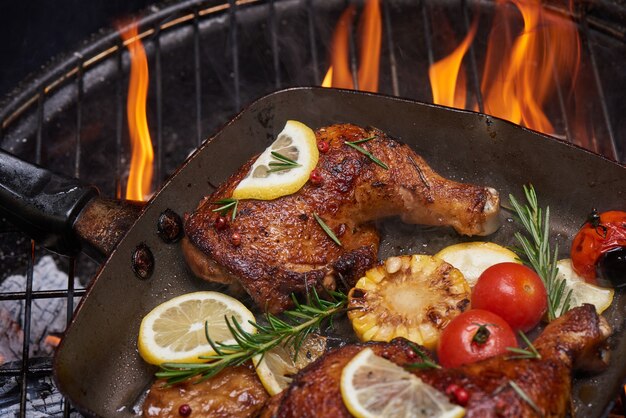 Grilled chicken legs on the flaming grill with grilled vegetables with tomatoes, potatoes, pepper seeds, salt.