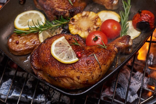 Grilled chicken legs on the flaming grill with grilled vegetables with tomatoes, potatoes, pepper seeds, salt.