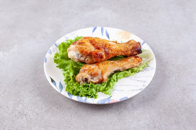 Grilled chicken legs meat with lettuce on white plate