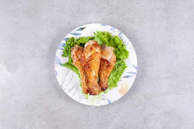 Grilled chicken legs meat with lettuce on white plate