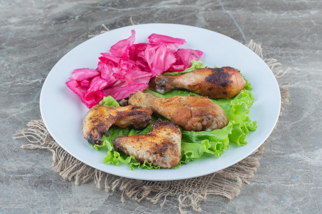 Куриное мясо на гриле и маринад с листьями салата на белой тарелке.