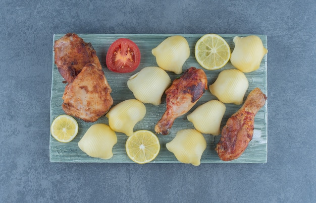 Части курицы-гриль и отварной картофель на деревянной доске.