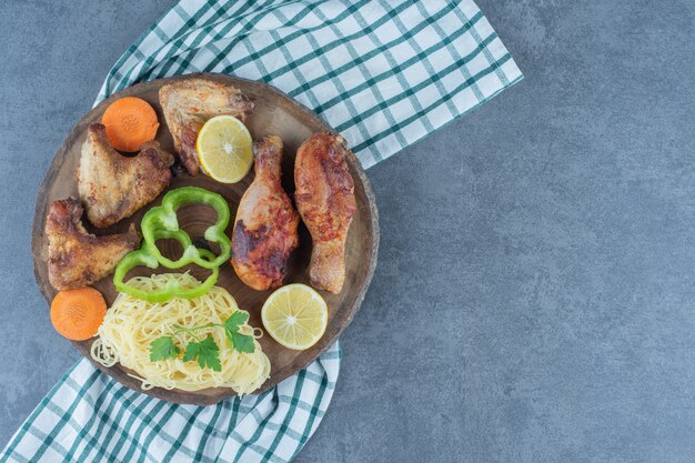 Grilled chicken parts and spaghetti on wood piece.