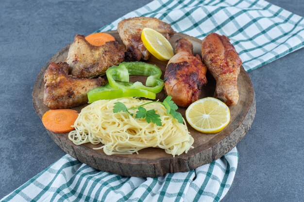 Жареные куриные части и спагетти на деревянной доске.