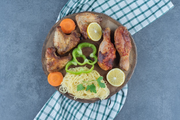 Grilled chicken parts and spaghetti on wood piece. 