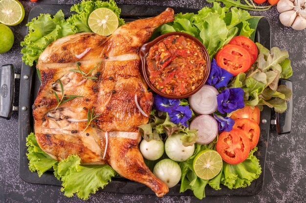 Grilled chicken on a plate with chili peppers, garlic sauce and sprinkled with pepper seeds.