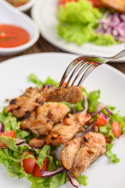 Grilled chicken on a white plate with a salad of tomatoes, carrots and chilies cut into pieces.