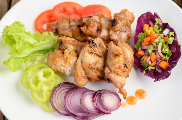 Grilled chicken on a white plate with a salad, tomatoes, red onion, and chilies cut into pieces on wooden table.