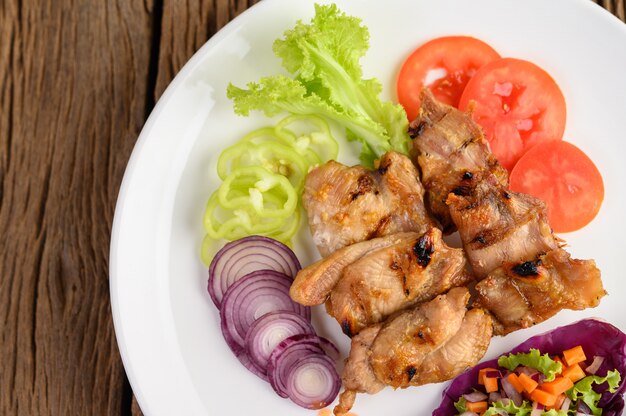 Grilled chicken on a white plate with a salad, tomatoes, red onion, and chilies cut into pieces on wooden table.