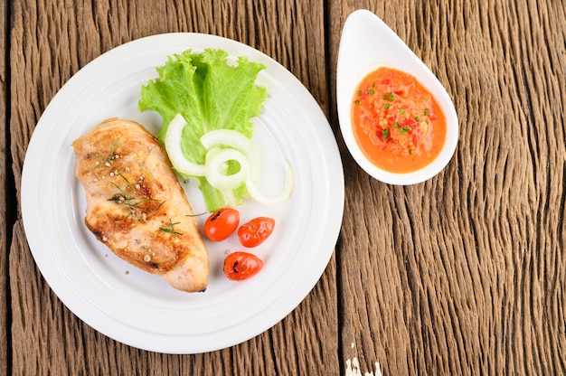 Free photo grilled chicken on a white plate with tomatoes, salad, onion and chili sauce.