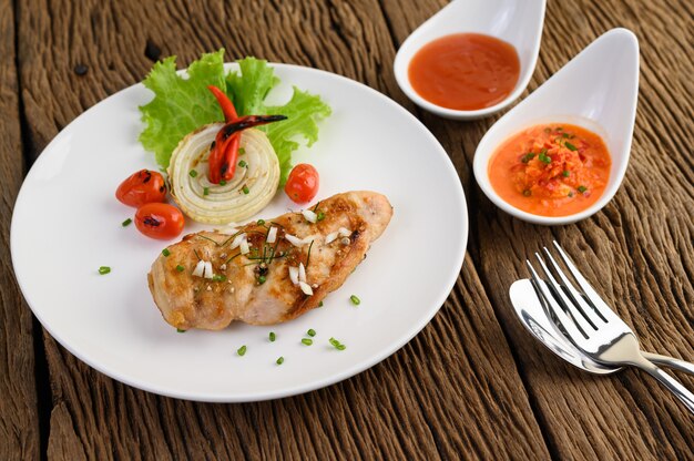 Grilled chicken on a white plate with tomatoes, salad, onion, chili and sauce.