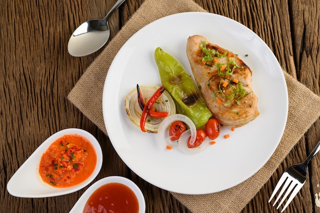 Grilled chicken on a white plate with tomatoes, salad, onion, chili and sauce.