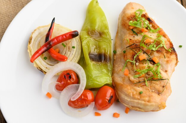 Жареная курица на белой тарелке с помидорами, салатом, луком, чили и соусом.