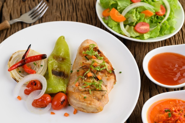 Grilled chicken on a white plate with tomatoes, salad, onion, chili and sauce.