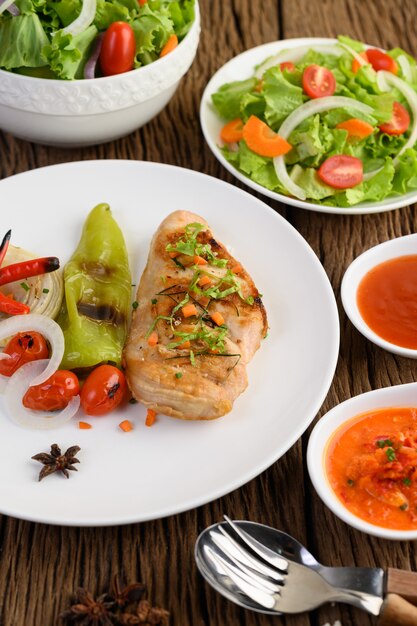 Жареная курица на белой тарелке с помидорами, салатом, луком, чили и соусом.