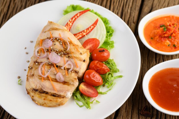 Grilled chicken on a white plate with tomatoes, salad, onion, chili and sauce.