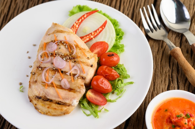 Grilled chicken on a white plate with tomatoes, salad, onion, chili and sauce.