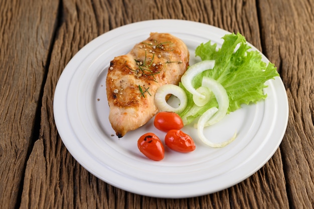 Grilled chicken on a white plate with tomatoes, salad and onion.