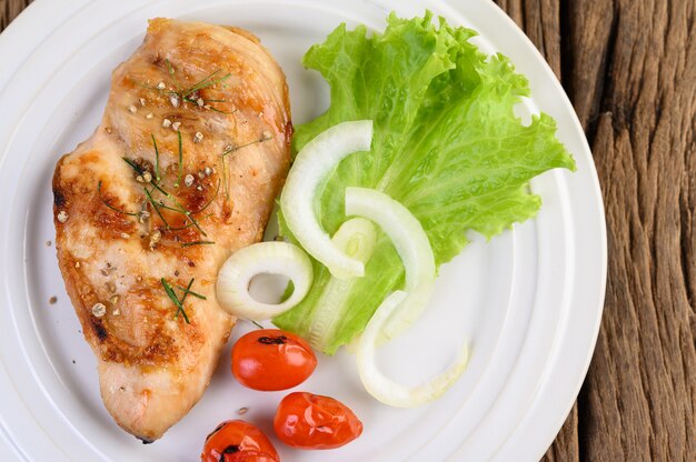 Grilled chicken on a white plate with tomatoes, salad and onion.