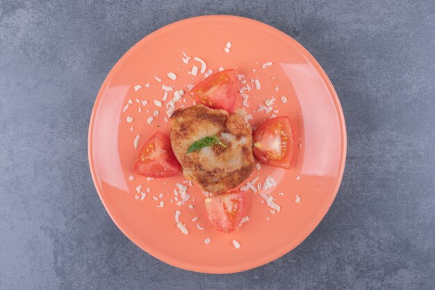 Foto gratuita pollo alla griglia con fette di pomodoro su piastra arancione.