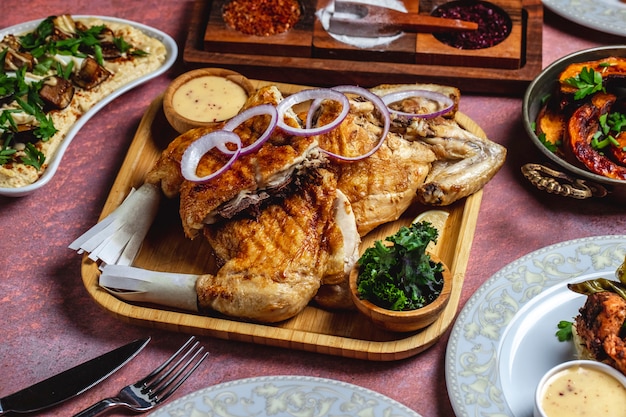 Grilled chicken on the wooden board lettuce onion sauce side view