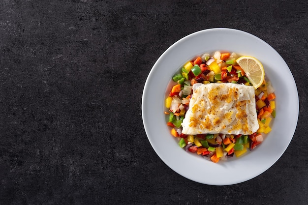 Grilled cod with vegetables in plate on black stone background
