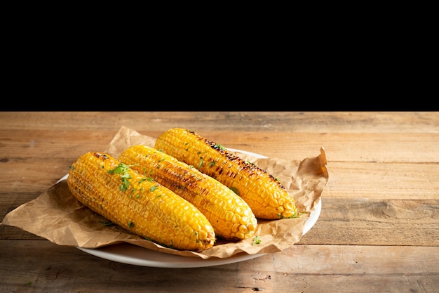 Grilled corn cobs on wood background.