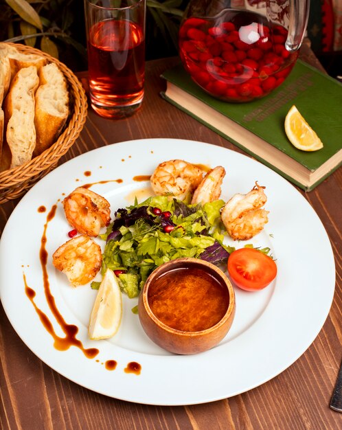 Grilled crevettes with green salad, tomatoes, lemon and dip sauce in white plate.