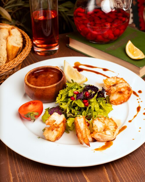 Grilled crevettes with green salad, tomatoes, lemon and dip sauce in white plate   