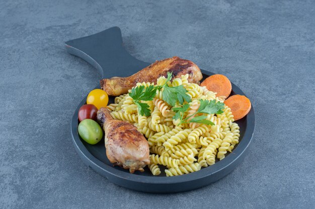 Grilled drumsticks and fusilli pasta on wooden board.