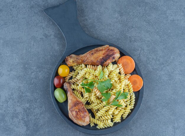 Grilled drumsticks and fusilli pasta on wooden board. 