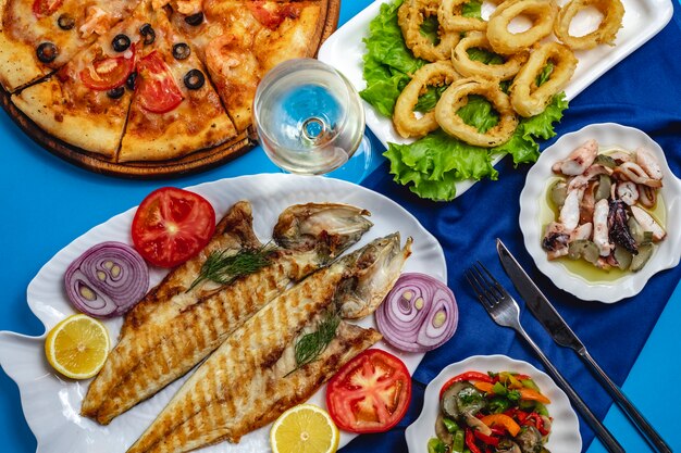 Grilled fish onion tomato calamary green salad top view