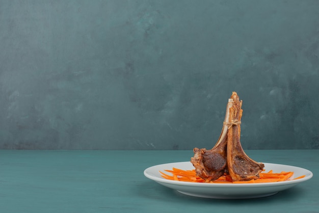 Grilled lamb chops on white plate with carrot slices.